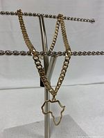 Gold colour chain necklace with Africa pendant displayed on a necklace stand against white background.