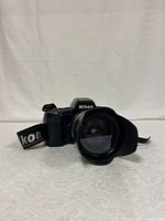 Front angled view of Nikon F90X camera with attached Tamron lens showing the lens hood and Nikon branded strap.