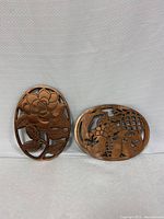 Two vintage metal trivets with decorative motifs, placed side by side on a white surface