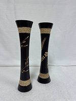 Two tall slim mango wood vases side by side on white fabric background showing carved designs and twine wraps