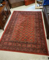 Photo showing full view of red patterned area rug placed on light-colored floor between furniture.
