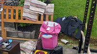 Overview of lot showing leather-look carry-on bags, children's jackets hanging on railing, patterned curtains draped on wooden frame, and various smaller bags on ground.