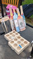 Wooden beverage boxes with handles and wooden beverage signs shaped like whiskey bottles set on the ground outdoors.
