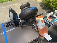Photo showing an electric iron with cord and a disassembled ceiling fan motor housing with mounting hardware on a table.