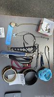 Photo showing an assortment of costume jewelry including necklaces with chains and fabric bands, bracelets, bangles in black and gold-tone finishes, with some items having clasps and charms.
