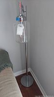 Full view of the tall metal floor lamp with clear glass jar-like globe attached near the top, standing beside a couch on a wooden floor.