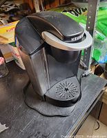 Keurig K-Classic K50 coffee maker in black showing water reservoir, drip tray, and power cord on a table.