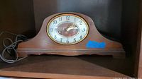 Full view of the Revere electric mantel clock showing wooden curved case, electric cord, and clock face with glass and brass bezel.
