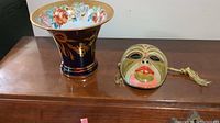 Photo of Limoge vase paired with a brass mask on a wooden surface.