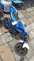 Full view of mini-bike showing the entire bike painted blue with white fender, visible engine, and damaged seat.