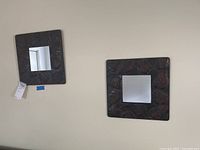 Two square mirrors with embossed tin frames featuring leaf patterns displayed on a table.