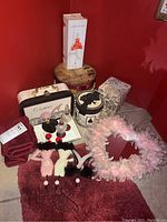 Assorted glass perfume bottles, decorative boxes, burgundy towels, hooks, and feather heart mirror all displayed on a flat surface against a red wall.
