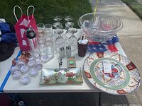 Comprehensive photo of all items on a white table outside including glassware, bowls, plates, shaker, tray, salt and pepper shakers, napkin rings.