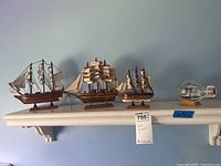 Four wooden model sailing ships on a wall shelf, varying sizes and rigging detail, including one in a bottle.
