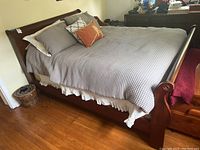 Full view of wooden sleigh bed frame with gray waffle comforter and pillows on wood floor