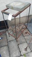 Full view of metal table/stand with concrete slab on top, showing rust and wear.