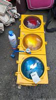 Front view of yellow Econolite traffic signal light with red, yellow, and blue lenses and EZ Chill refrigerant oil can with pressure gauge beside it on pavement.