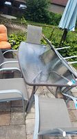 Overview of rectangular glass-topped metal patio table surrounded by six metal frame mesh chairs on stone patio.