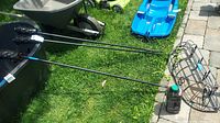 Three metal torches laid on a lawn with bottle of torch fuel and one hanging rack visible. Torches have woven torch heads and long black metal handles.