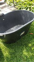 Black oval plastic tank outdoors with drain valve and two fittings visible. Shows general exterior condition including sticker label on side.