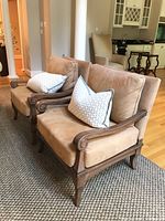 Two matching wood framed beige upholstered accent chairs with decorative pillows, side angle view showing the wooden armrest design and fabric texture.