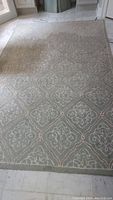 Full view of green area rug with geometric floral pattern on light floor.