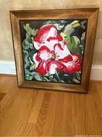 Full view of framed floral painting resting on wooden floor, showing gold-toned frame and flower artwork.
