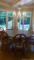 Full dining set around a round wooden table under chandelier seen through large windows.