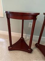 Front and side view of the round wooden end table showing the three legs with brass accents and the triangular base shelf.