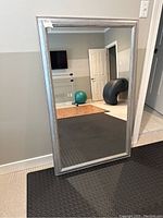 Full view of the large silver-toned framed mirror standing on floor against a wall, showing its size and condition in a room setting.