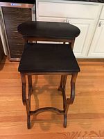 Pair of black-topped wooden nesting tables with ornately designed wooden bases in a kitchen setting, showing size relationship: smaller table nested under larger table.