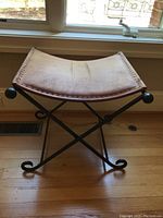 Side angle view of saddle seat showing leather upholstery and metal crossed base.