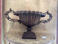 Front view of the dark metal urn showing scalloped rim, ribbed body, and detailed handles.