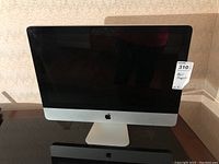 Front view of Apple iMac showing black screen, silver aluminum chassis and Apple logo on front.
