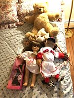 Wide shot showing all items on bed including boxed Barbie Doll, Red Sox Marionette Doll, and assorted plush toys