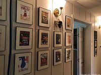 Hallway wall with multiple framed Broadway show cover posters and two opera masks mounted next to them.