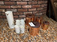 Photo displaying four copper-tone vintage canisters with lids alongside a white ceramic pitcher and six ceramic glasses, all with matching decorations of birds on a bicycle.