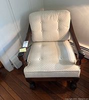 Front view of the upholstered wood armchair showing cream patterned cushions with button tufting and dark wood frame.