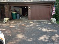 Wide shot showing the pair of concrete lion statues placed on either side of a driveway in front of a garage, giving scale and setting context.
