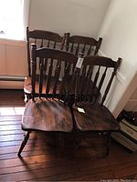 Four solid wood dining chairs grouped together, showing dark brown finish and spindle backs.