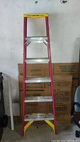 Full length view of the red and yellow Werner fiberglass step ladder with aluminum steps, showing 6 foot height.