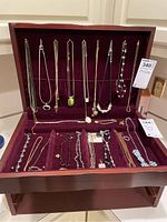 Wide shot of wooden jewelry box with burgundy velvet lining holding all necklaces