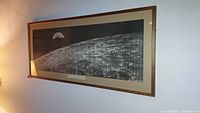 Wide view of the framed black and white printable photograph showing Earth from deep space above the lunar surface, hanging on a wall over a couch.