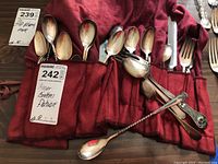 Silverplated spoons and forks rolled in red cloth with MaxSold tags visible.