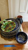 Stack of ten navy-blue speckled plates topped with a green leaf-shaped plate and a small blue bowl