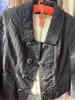 Black textured women's jacket with gold decorative buttons hanging, showing front detail and collar.
