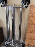 Metal clothing rack folded or disassembled showing shiny tubular frame and wheels.