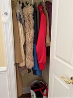 Closet view showing multiple hanging coats and jackets including beige, shaggy fur vest, and red jacket visible