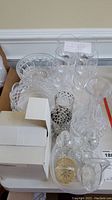 Wide view of assorted crystal glassware including candy dishes, glasses, and vases on table with white wall background.