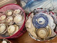 Various fine china pieces in two containers showing a mix of floral and blue Willow designs.